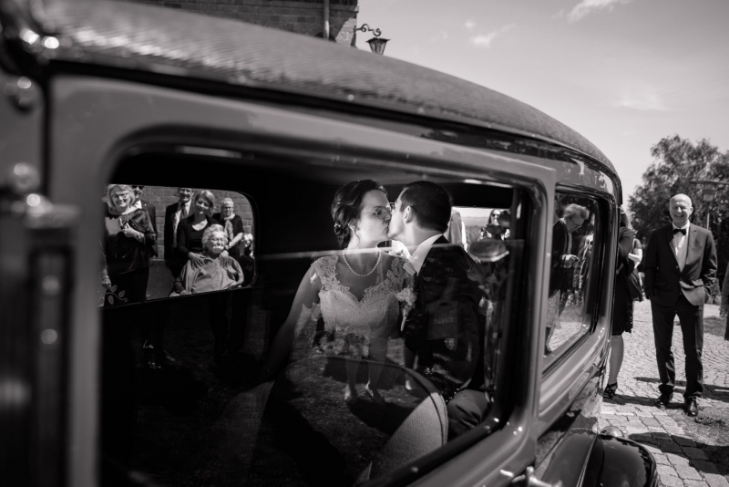 Bryllupsfoto. Brudepar kysser i bil. Billede skudt igennem halvåben bilrude